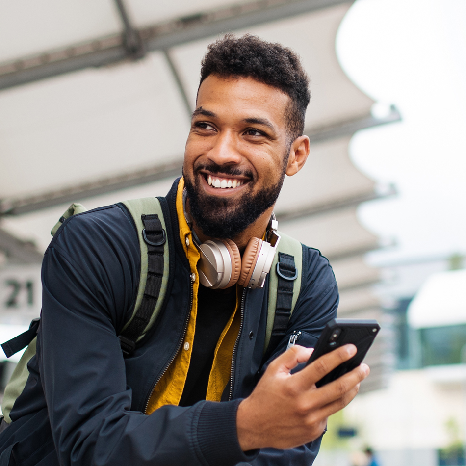 Man with backpack and headphones, holding phone and smiling
